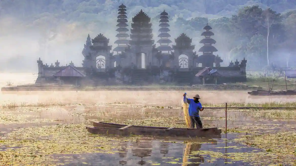 Visser op Tamblingan meer, met tempel op de achtergrond.