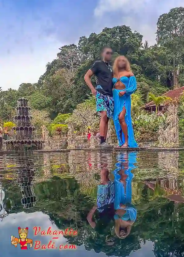 Stel poseert op de rand van de vijver in Tirta Gangga, met hun spiegelbeeld in het water